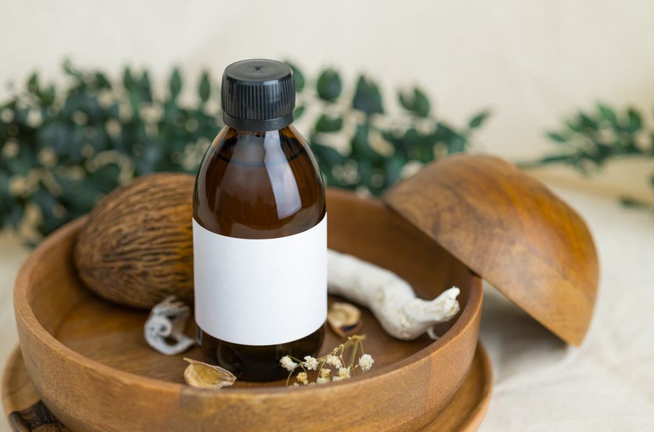 A brown glass bottle with a blank label placed on a wooden plate surrounded by botanical e
