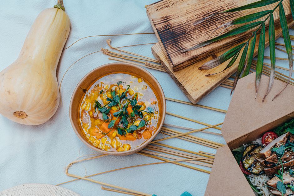 A cozy flat lay of a rustic table setting featuring a bowl of pumpkin soup and grilled foo