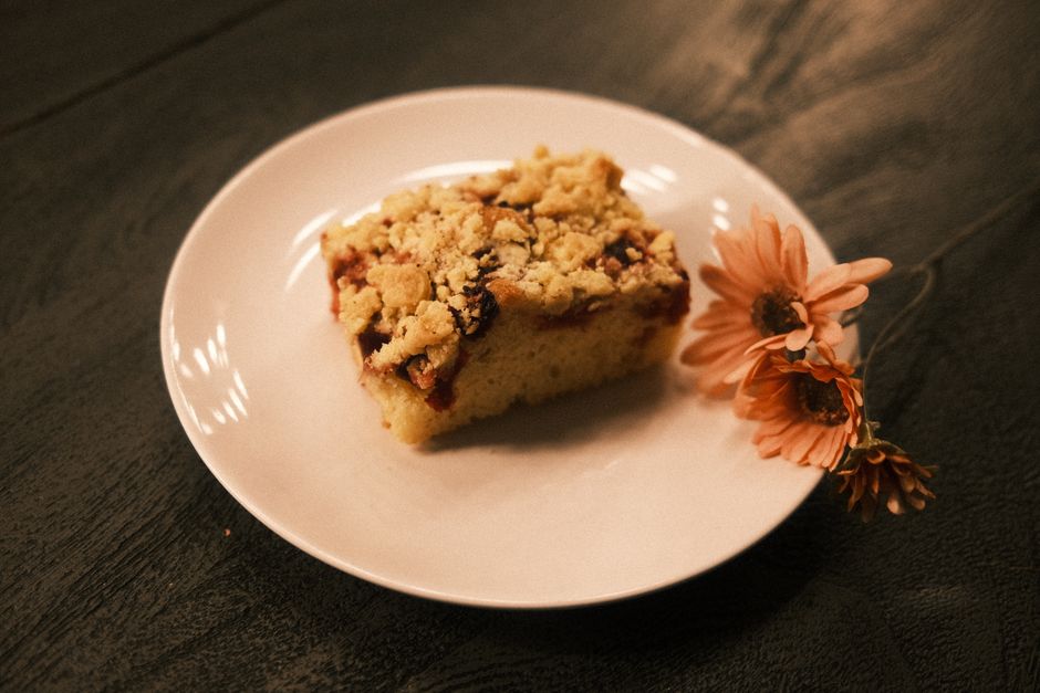 A piece of crumb-topped cake on a white plate with pink flowers for decoration.