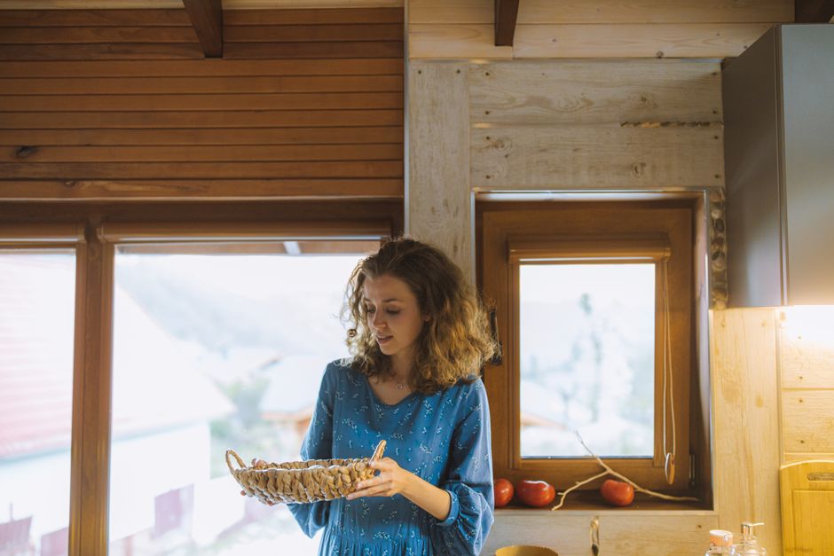 Woman in blue dress holding a wicker basket in a wooden interior by a window.